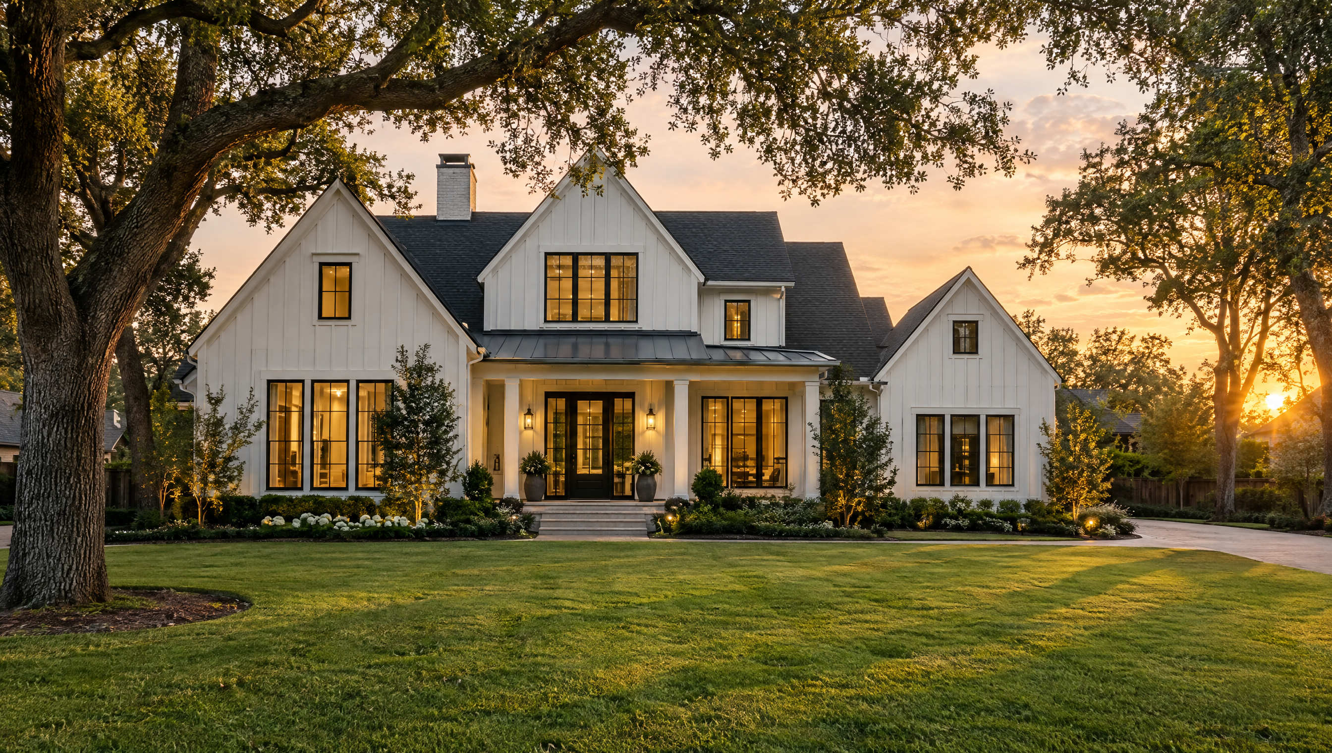 White modern farmhouse with a wide lawn and oak trees at golden hour